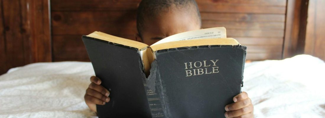 Young child reading a Holy Bible indoors, conveying a serene and religious atmosphere.